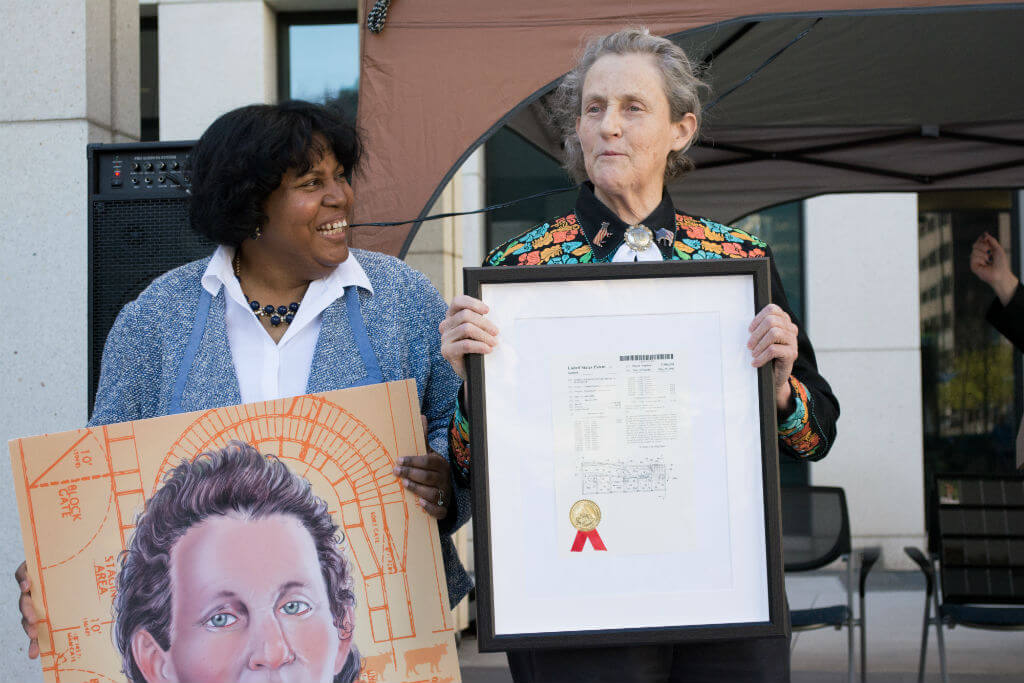 Image: Grandin holds up patent no. 5,906,540 for her invention of an animal stunning system, while Joyce Ward from USPTO’s Office of Education and Outreach (left) presents Grandin with an oversized copy of an inventor trading card depicting Temple and her livestock handling designs.