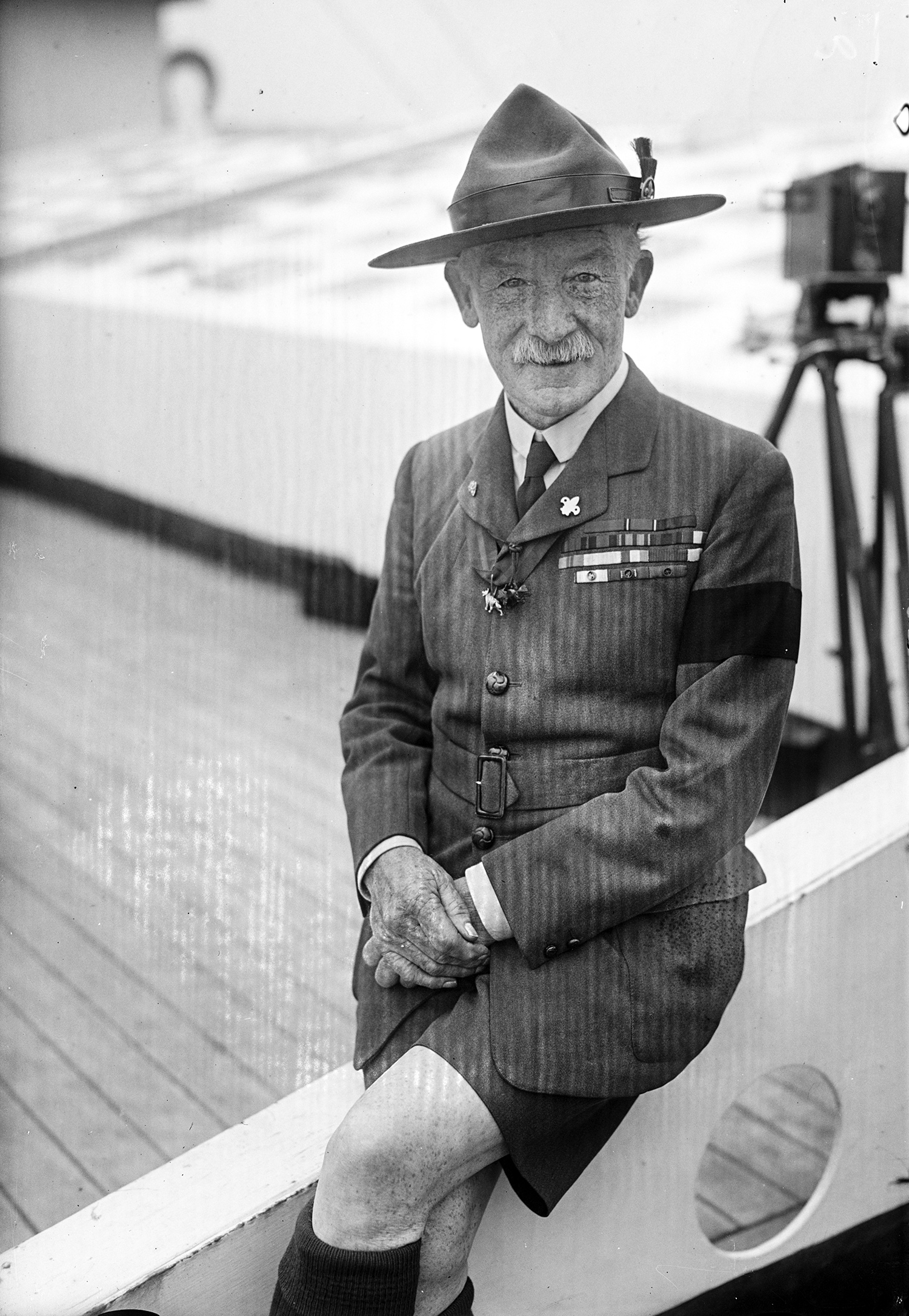 Robert Baden-Powell, smiling, in uniform and wearing military decorations on his chest and a wide-brimmed hat, photographed on the roof of a building.