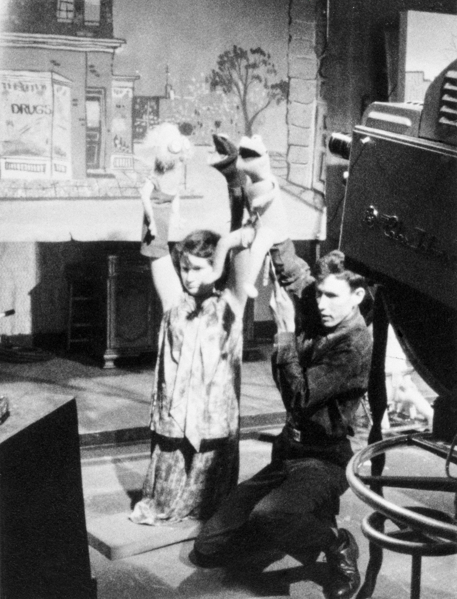 Jim and Jane Henson on their knees performing with their puppets in front of a television camera and television monitor on the set of “Sam and Friends.”
