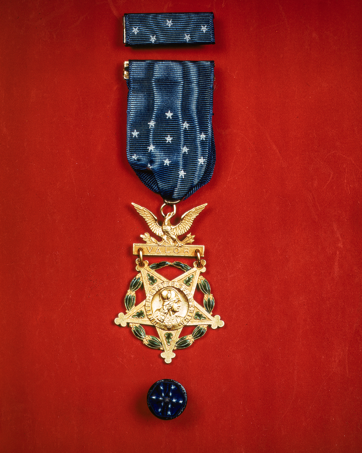 The Medal of Honor, which consists of a five-pointed star with the helmeted goddess Minerva in the center, encircled by a wreath, suspended from a blue ribbon with a gold bar reading “Valor.” 