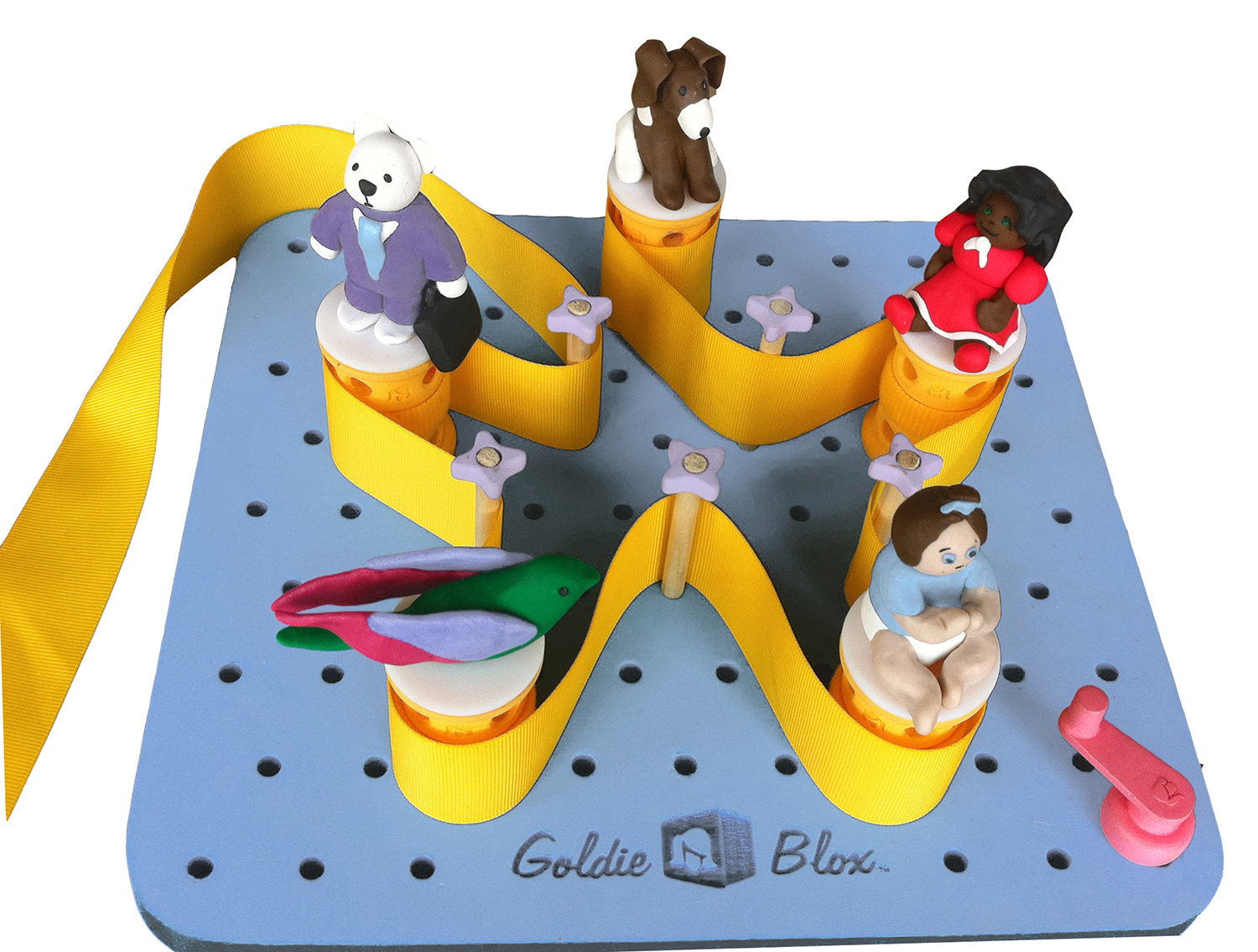 Blue pegboard with GoldieBlox logo. Cylinders topped with clay figurines and wooden dowels are inserted into the holes, and a ribbon is strung around them forming a star shape. There is a crank in the corner of the pegboard.