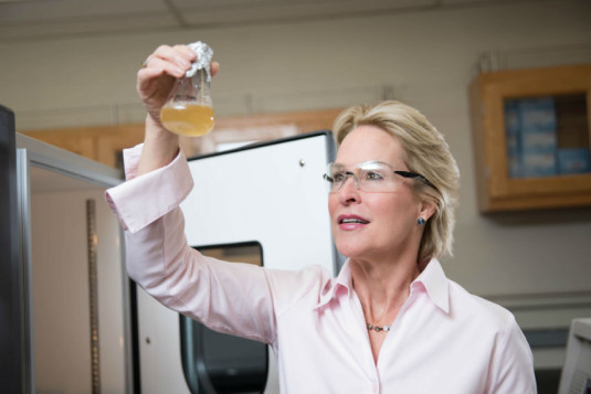 Image: Chemist Frances Arnold holds a beaker with yellow liquid up to the light.