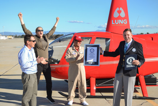 Martine Rothblatt(excitedly jumping)  and the team from Tier one engineering proudly celebrating in front red Electric helicopter that, with the word lung written on it, huge smile, that just set  Guinesss World Record  being awarded plaque
