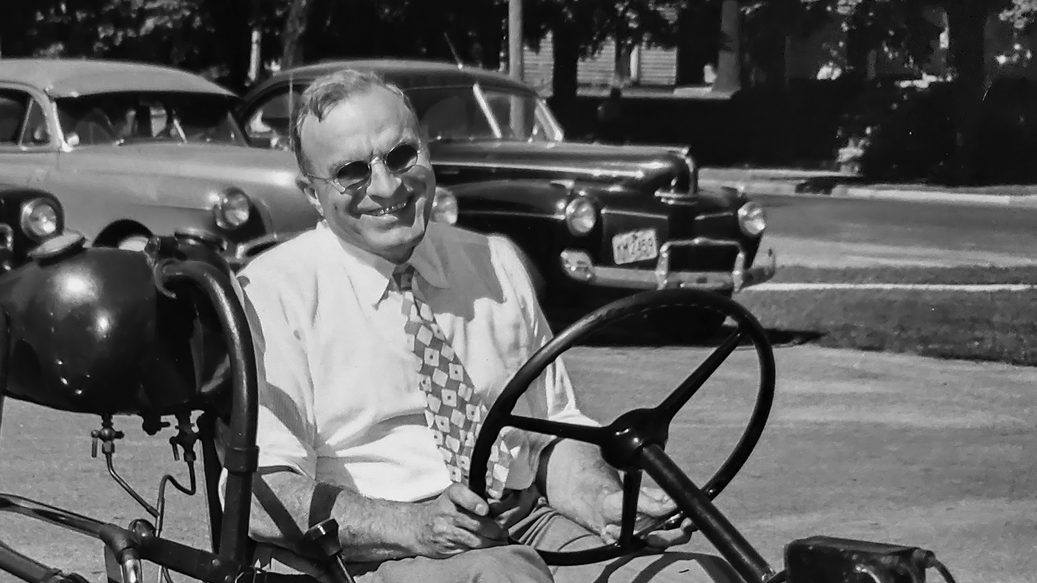 Man wearing white dress shirt and tie sitting in open-roof car. 