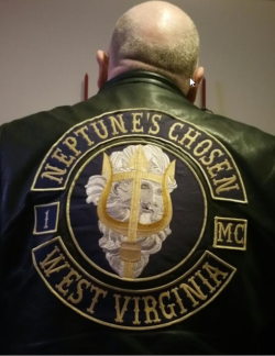 Back of a man wearing a leather jacket with the log for Neptune’s Chosen motorcycle club from West Virginia showing image of Neptune in center of circle 